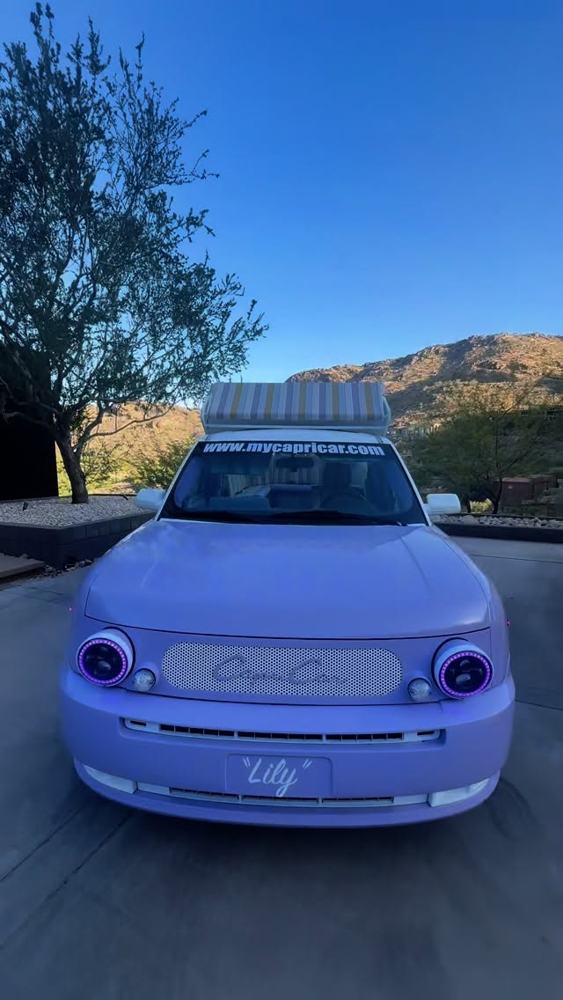 The lavender Capri Car driving toward the camera on a desert road